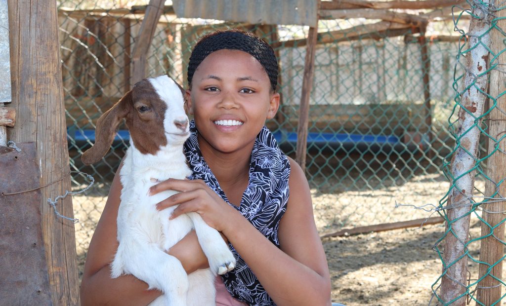 A girl smiling and holding a baby goat.